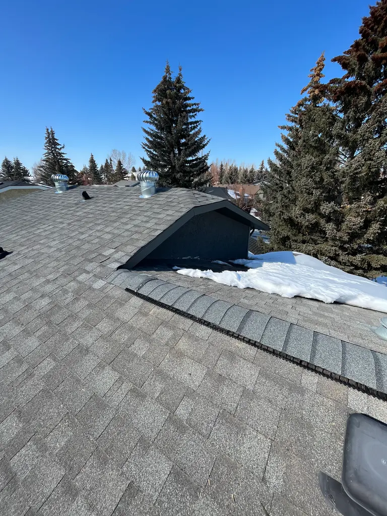 Ice damming at the eaves alongside a new continuous ridge vent installed for better ventilation on a low-slope 3:12 Calgary roof