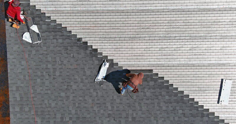 two body strapped roofers standing on a house and installing asphalt shingles