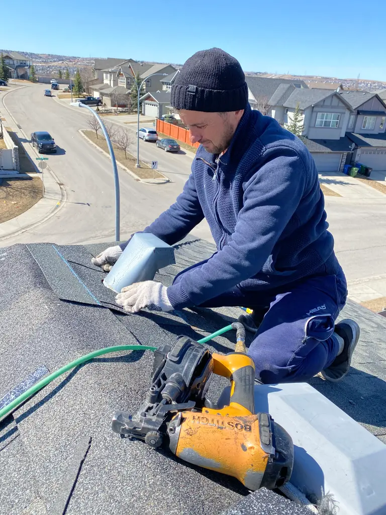 Sokol Preka nailing down asphalt shingles with a yellow nailing gun on a Calgary roof replacement